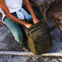 Olive green travel backpack on the ground with front zips and side strap details