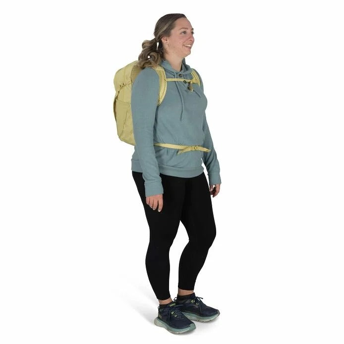 Person wearing a light blue hoodie, black leggings, and a beige backpack on a white background
