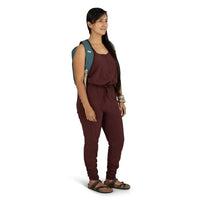 Woman wearing a maroon jumpsuit with a green backpack on a white background