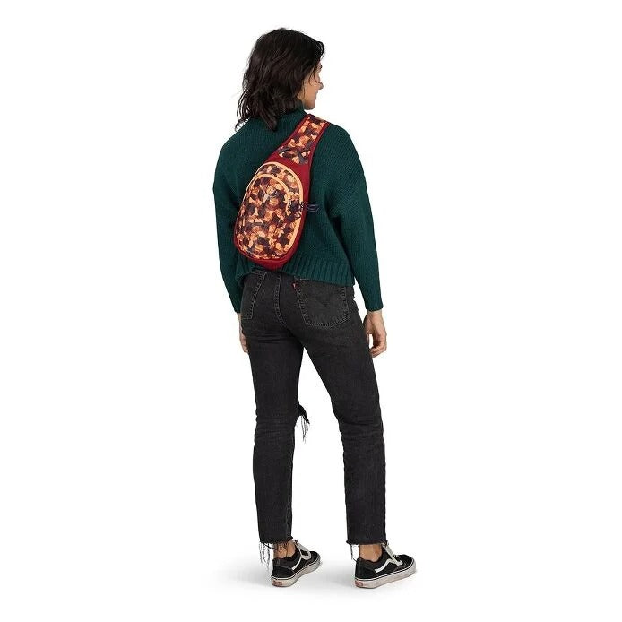 Person wearing a green sweater and black pants with a red and brown patterned bag on their back against a white background