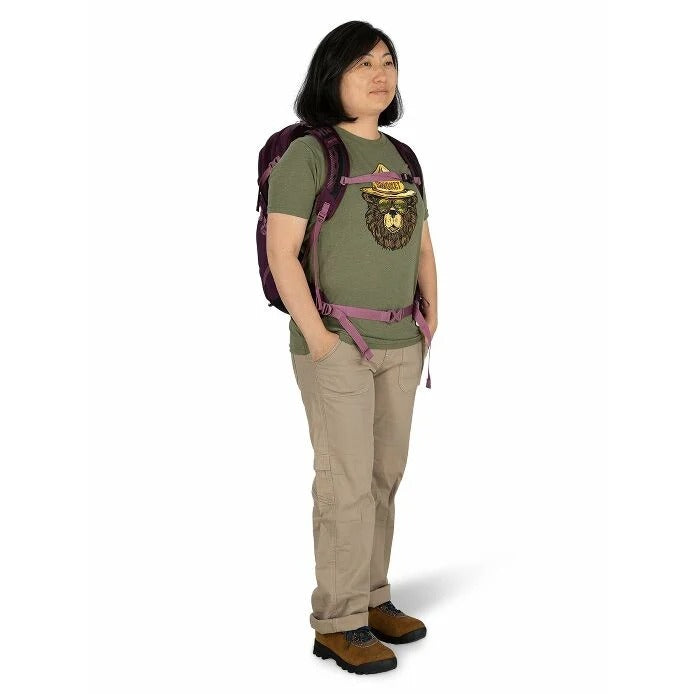 Person wearing a green t-shirt with a graphic design, beige pants, and a purple backpack on a white background
