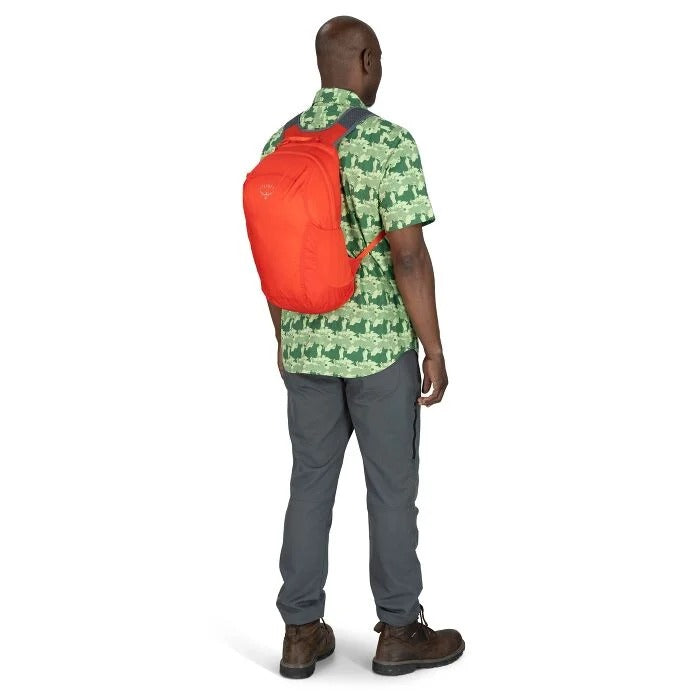 Person wearing a green patterned shirt, gray pants, and brown shoes with an orange backpack on a white background