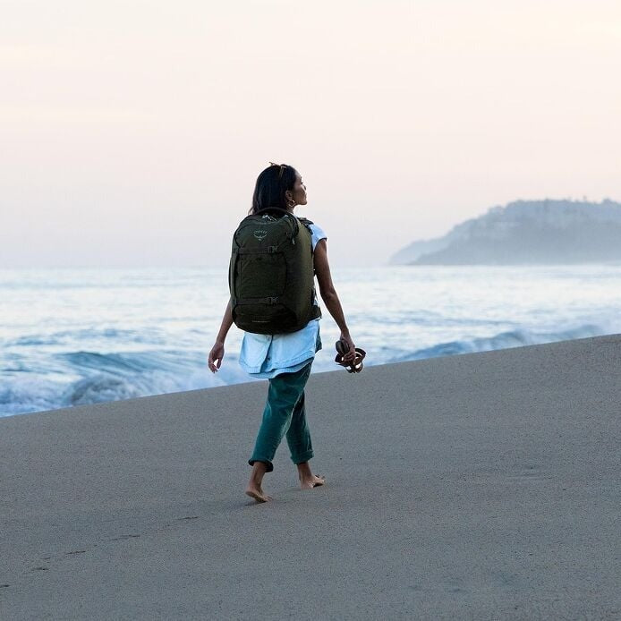 Green travel backpack on a person standing outdoors, viewed from the back