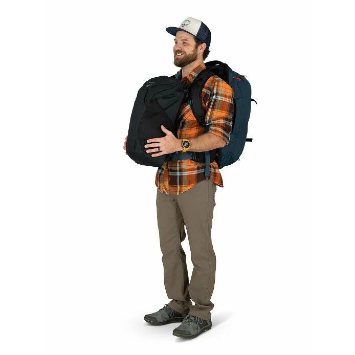 Man wearing a plaid shirt and cap, holding a black backpack with a blue backpack on his back against a white background.