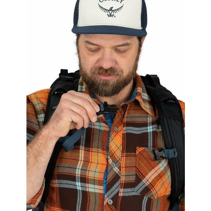 Man adjusting a backpack strap wearing a plaid shirt and a cap with a logo.