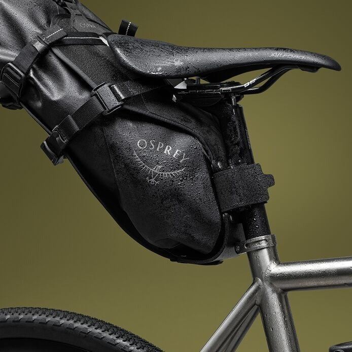 Black Osprey bike saddle bag attached to a bicycle frame with a greenish-brown background