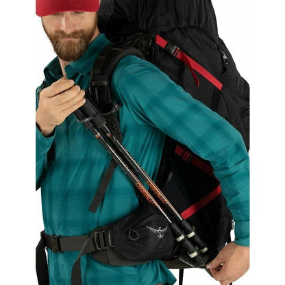 Man wearing a teal jacket with a black backpack and hiking poles on a white background