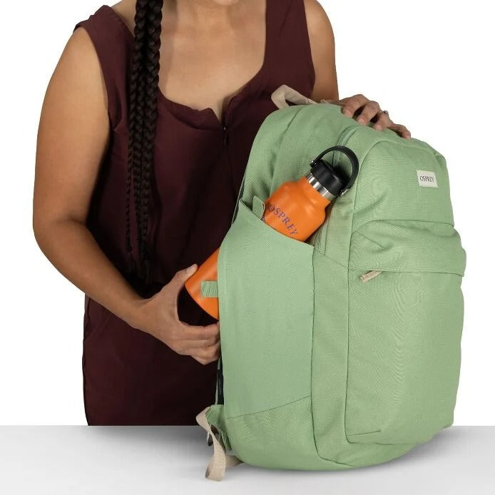 Green backpack with an orange water bottle held by a person on a white background
