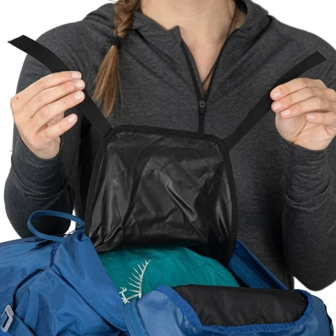 Person holding a black compression bag over a blue jacket on a white background