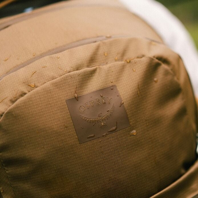 Brown backpack with a visible brand logo on a blurred natural background