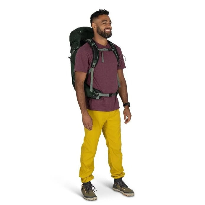 Man wearing a purple shirt, yellow pants, and a black backpack on a white background