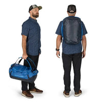 Man holding a blue duffel bag and wearing a matching backpack on a white background