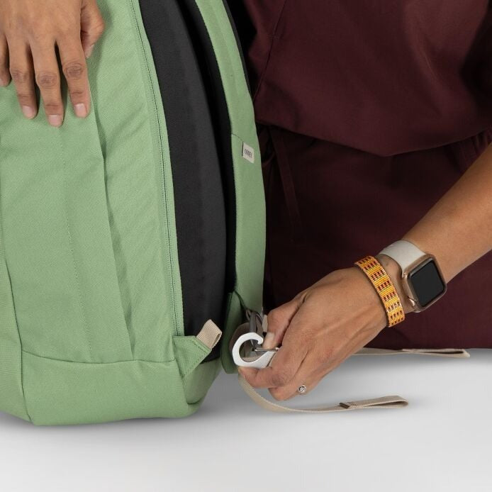 Person adjusting a green backpack strap on a light gray background