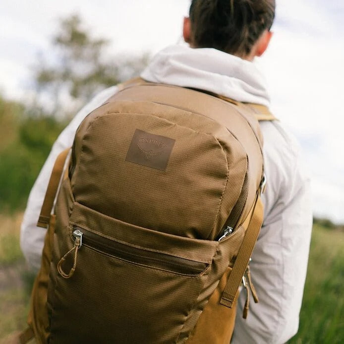 Person wearing a brown backpack outdoors with a blurred natural background