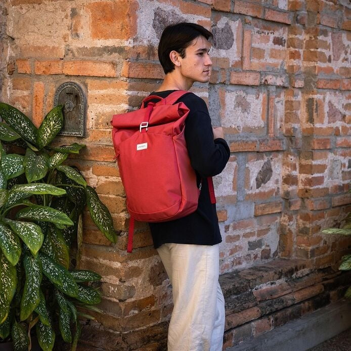 Person wearing a red backpack against a brick wall