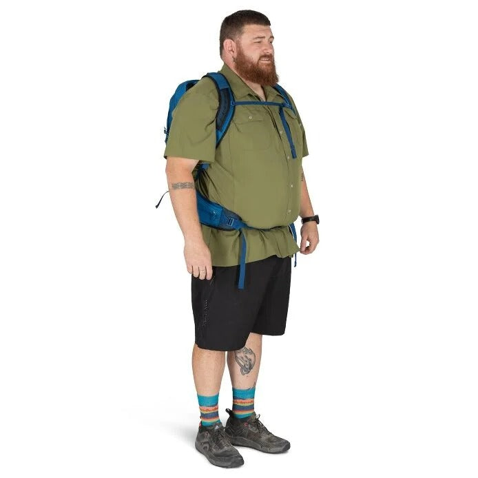 Man wearing a green shirt, black shorts, and hiking boots with a blue backpack on a white background